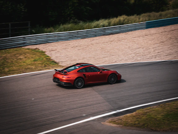 Hugo Becerra leaning into a sharp turn on a sunlit race track, red racing car vibrant against the black asphalt.