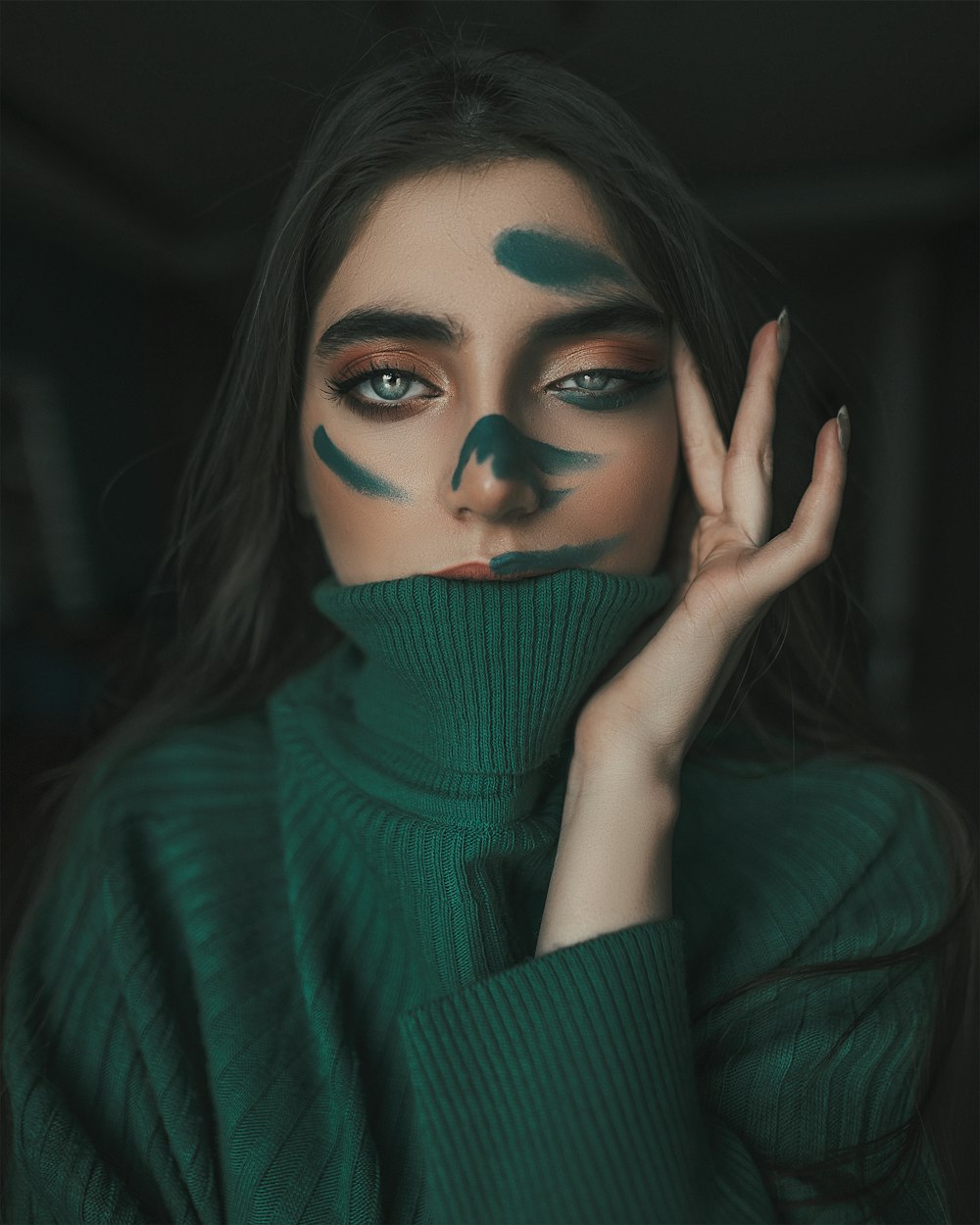 Frau im grünen Rollkragenpullover bedeckt ihr Gesicht mit der Hand