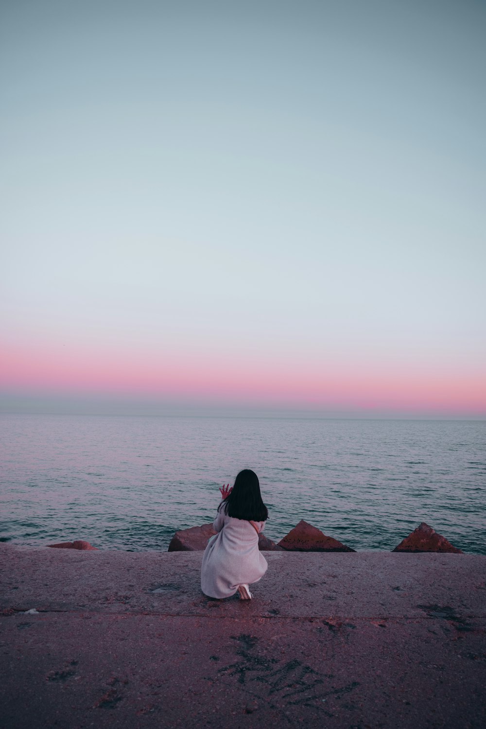 woman in white dress sitting on brown concrete dock during daytime