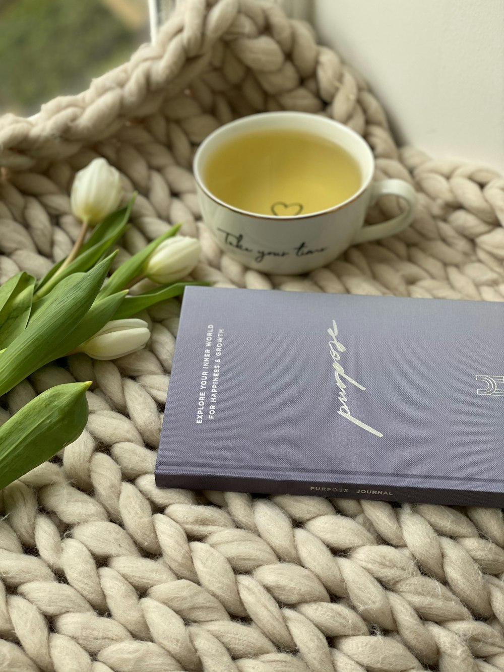 white ceramic mug beside black book on white textile