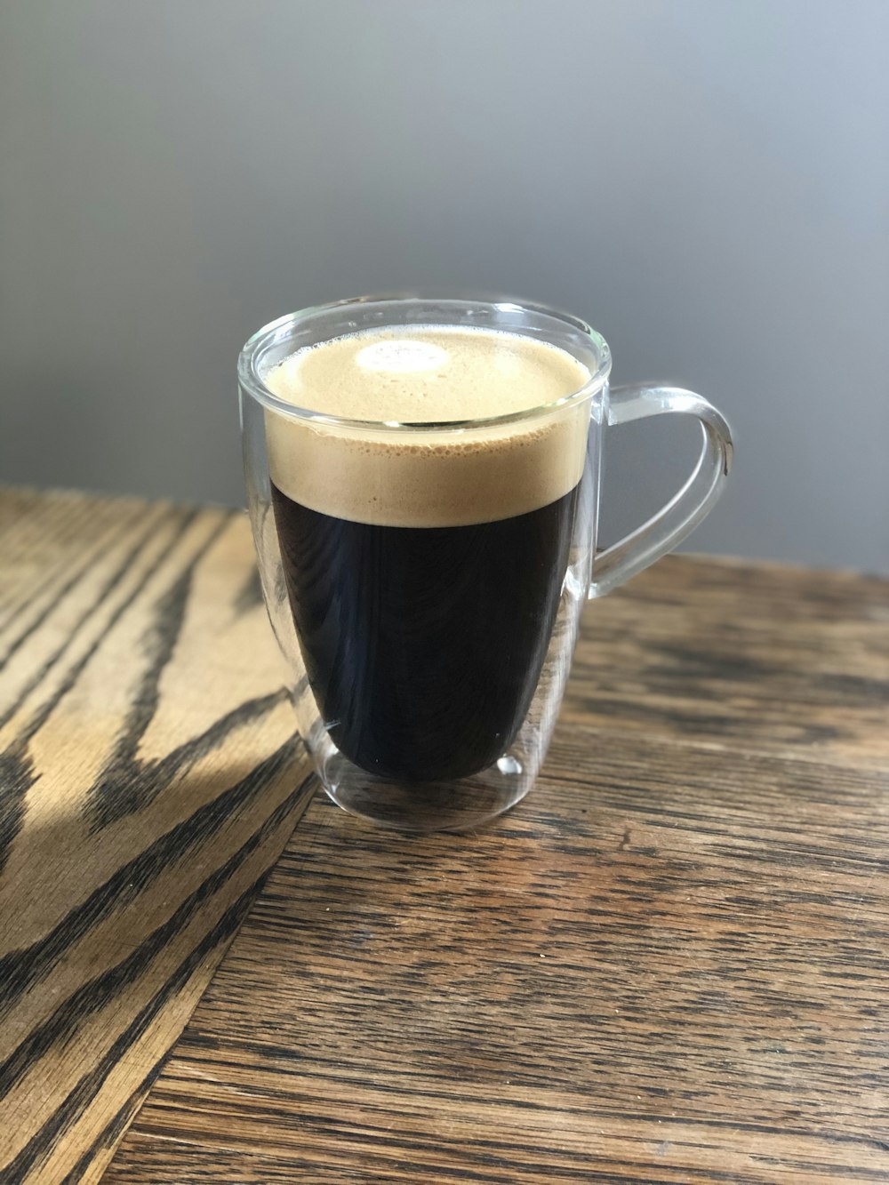 clear glass mug with brown liquid on brown wooden table