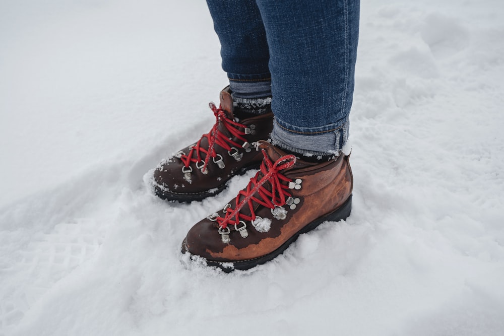 person in blue denim jeans and brown leather boots standing on snow covered ground during daytime