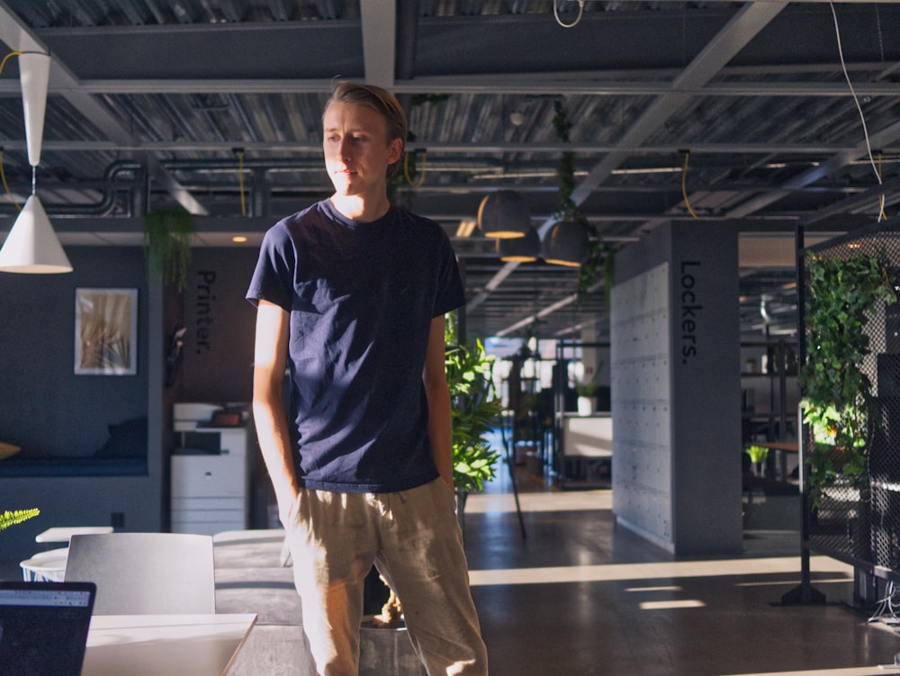 man in blue crew neck t-shirt and brown pants standing on brown wooden floor