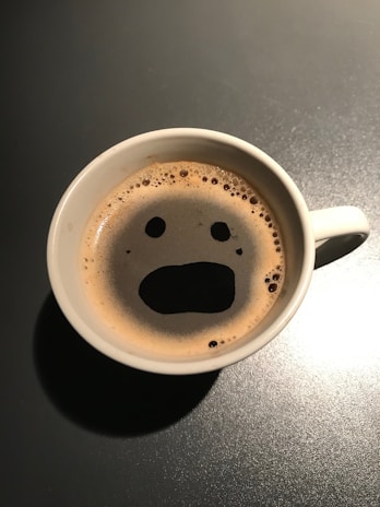 Close-up of a coffee cup with a detailed face print on the foam, held by a happy customer.