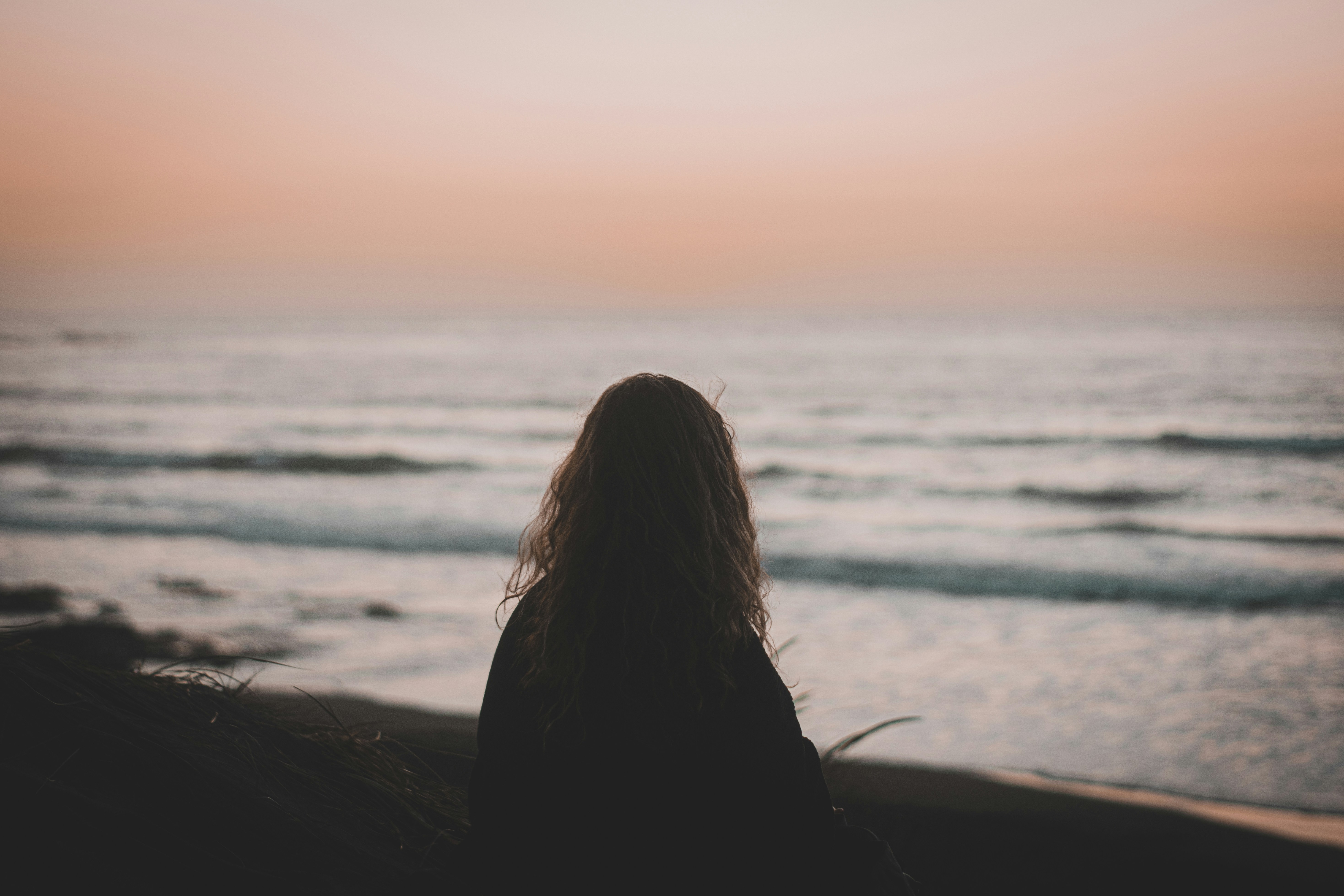 woman in black shirt sitting on beach during sunset