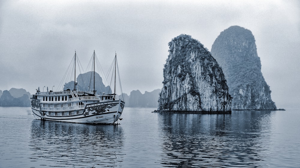 grayscale photo of boat on sea near mountain