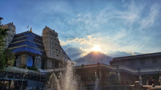 water fountain near brown building under white clouds and blue sky during daytime in ISKCON Temple Bangalore India