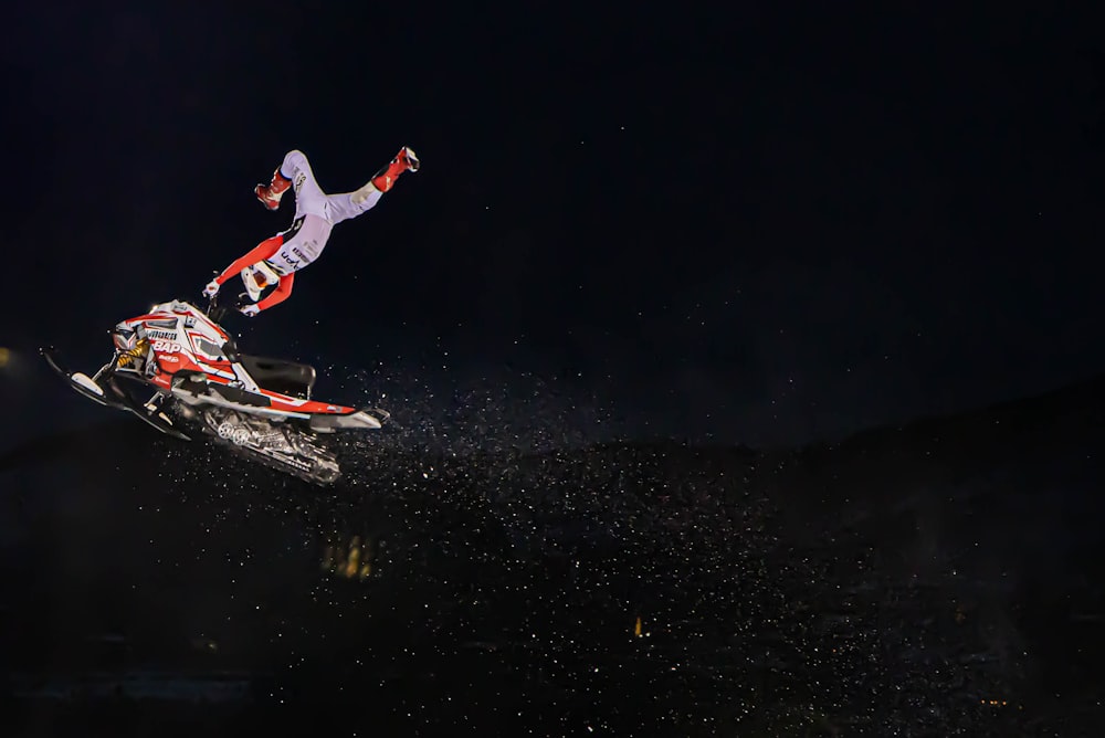 man in red jacket and white pants riding on red and white snowboard during nighttime