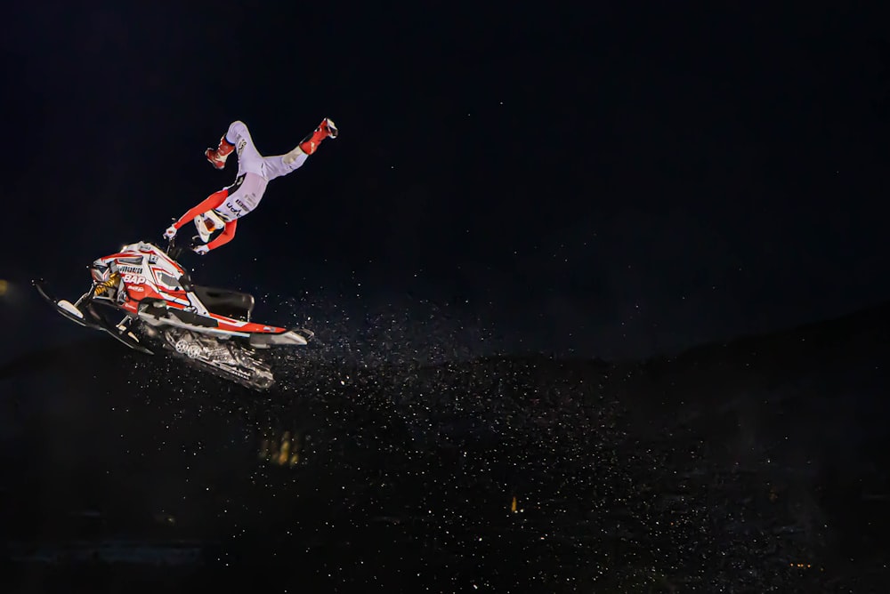 Hombre en chaqueta roja y pantalones blancos montando en snowboard rojo y blanco durante la noche