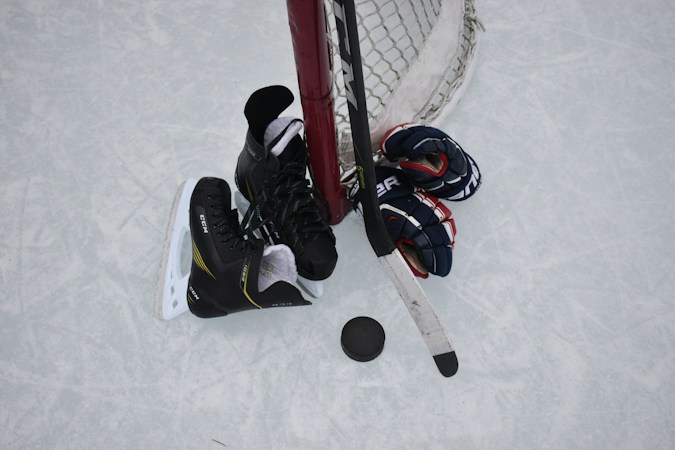 Hockey skates, gloves, a stick and a puck resting on the ice beside a goal net, ready for the Henderson Silver Knights season