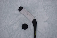 Close-up of a hockey puck sliding across the ice with players in the background.