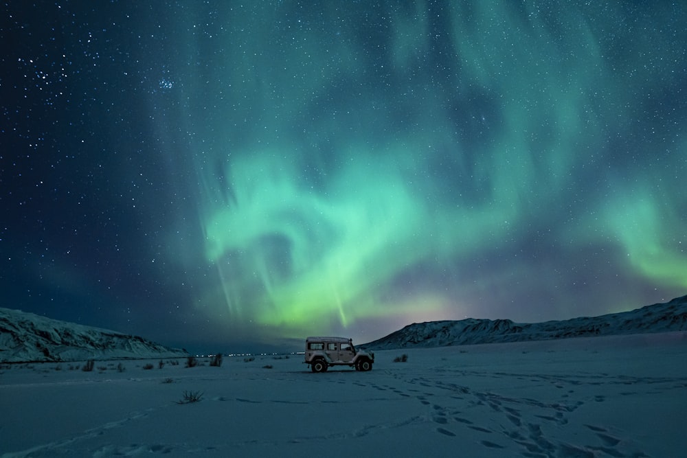 Schwarzer SUV auf schneebedecktem Feld unter grünen Aurora-Lichtern