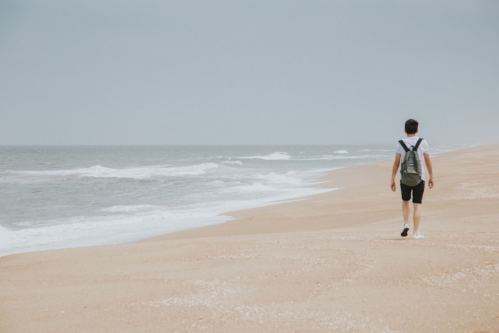 mulher na camisa preta e calças marrons andando na praia durante o dia