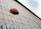 A football rests atop a barbed wire fence, positioned against the backdrop of a corrugated metal wall reaching up to a partly cloudy sky.