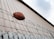 A football rests atop a barbed wire fence, positioned against the backdrop of a corrugated metal wall reaching up to a partly cloudy sky.