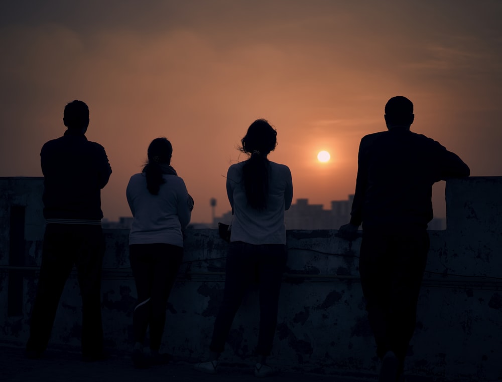 silhueta de 2 homens em pé na rocha durante o pôr do sol