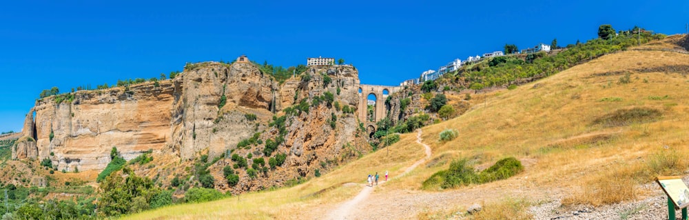 people walking on dirt road near brown rock formation under blue sky during daytime