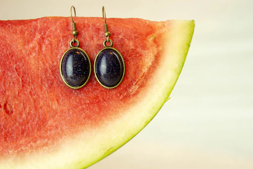Stylish imitation earrings set atop a glossy watermelon-red surface with soft lighting.