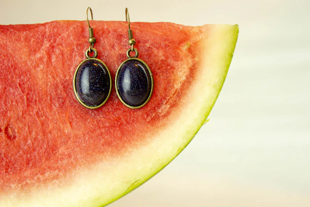 A smiling young woman showcasing melon’s trendy earrings against a peach watermelon background.