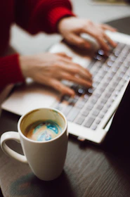 person holding white ceramic mug on white and black laptop computer