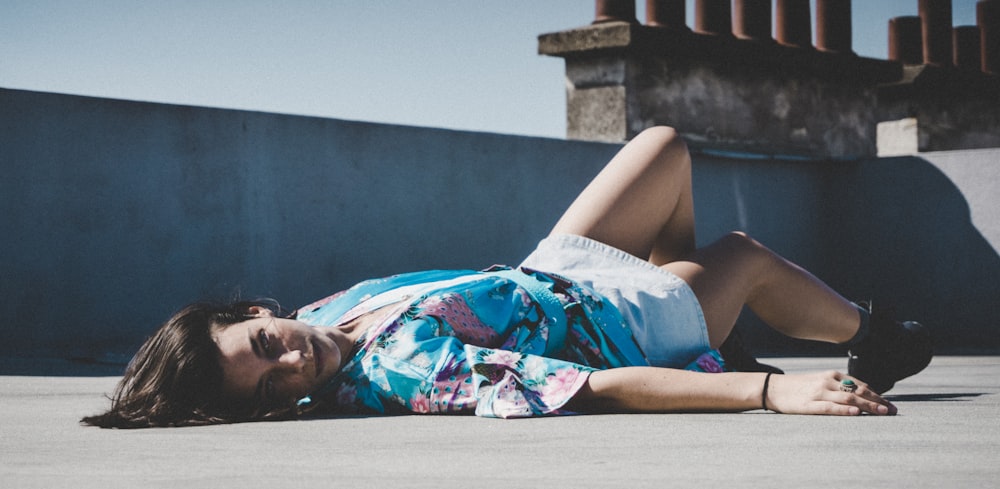 woman in blue white and red floral dress lying on gray concrete floor