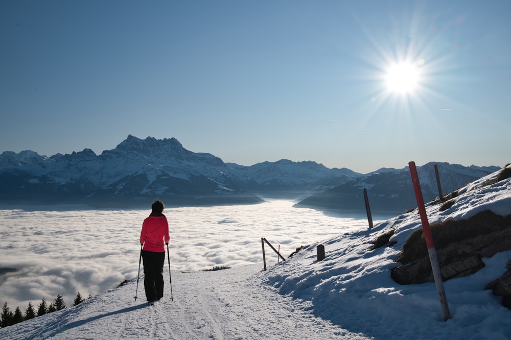 Persona in giacca rossa e pantaloni neri in piedi su terreno coperto di neve durante il giorno