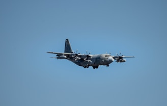 A military aircraft flying in a clear blue sky, showcasing its four propeller engines and robust design.