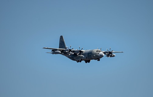 A military aircraft flying in a clear blue sky, showcasing its four propeller engines and robust design.