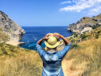 person in blue shirt and brown hat sitting on green grass field near body of water