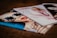Three glossy fashion magazines are spread out on a surface. The cover of the left magazine features a close-up of a person wearing striped sunglasses and red lipstick. The center magazine shows a blurred image of a person in light-colored clothing, while the right magazine is partially visible and monochromatic.