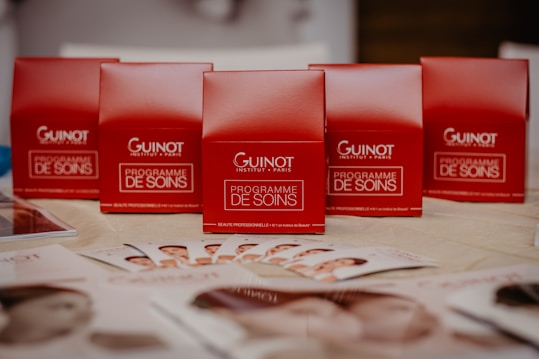 Several red boxes with 'Guinot Institut Paris' and 'Programme de Soins' written on them are arranged on a table. In the foreground, there are brochures displaying images of faces spread out on the table.