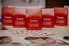 Several red boxes with 'Guinot Institut Paris' and 'Programme de Soins' written on them are arranged on a table. In the foreground, there are brochures displaying images of faces spread out on the table.