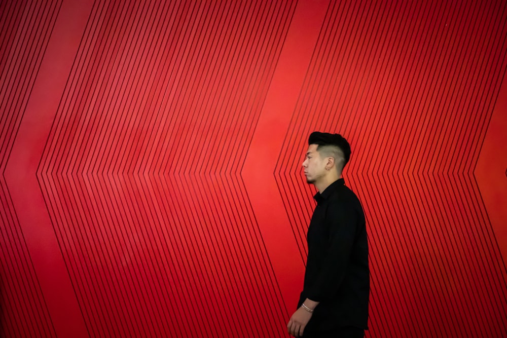 man in black long sleeve shirt standing beside red wall