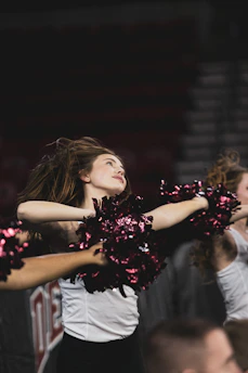 A vibrant cheerleader mid-jump wearing neon green and hot pink uniform under bright gym lights.