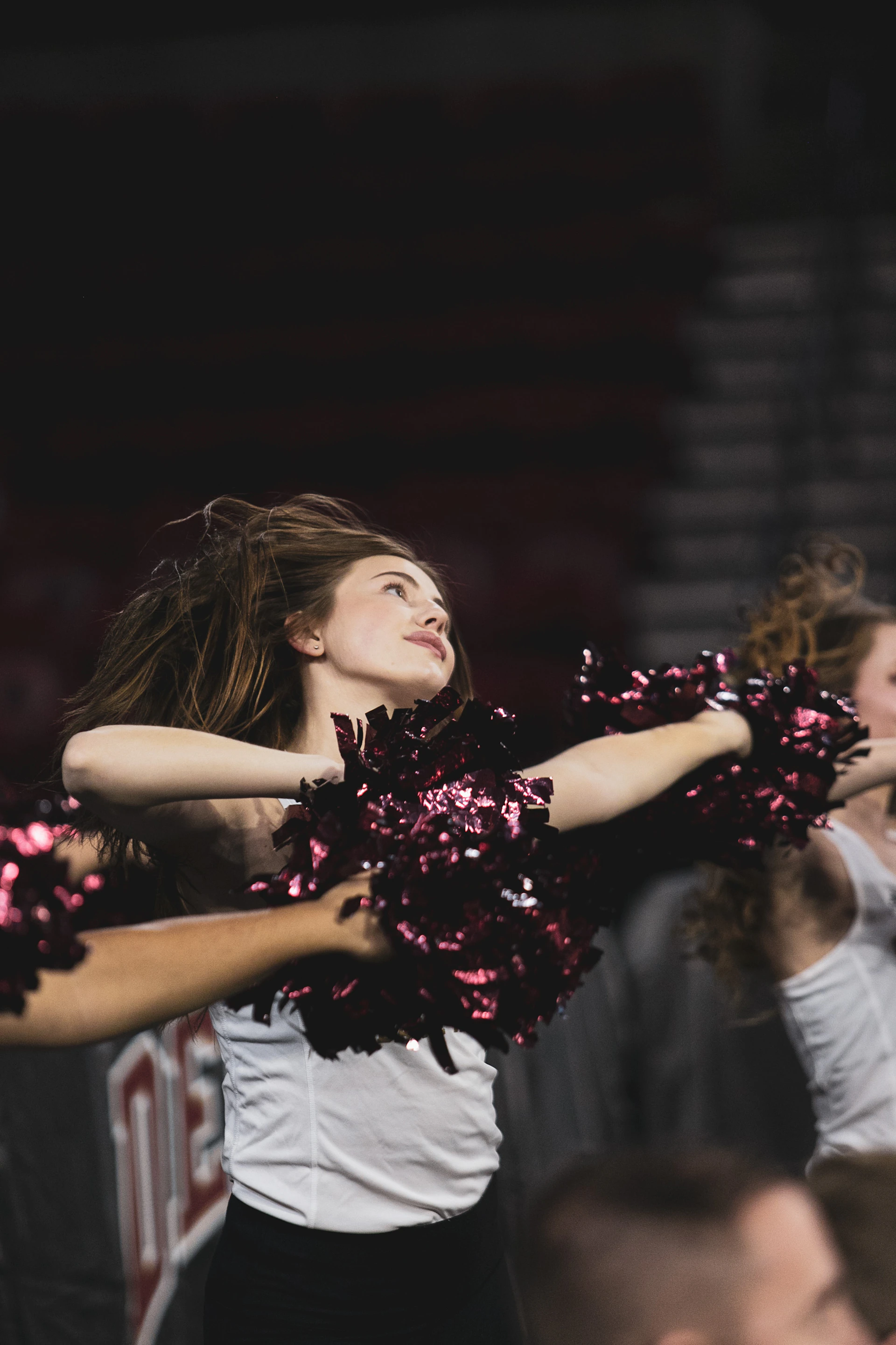 Close-up of a focused young athlete mid-cheer, her uniform shining under the gym lights with the vibrant club logo visible.