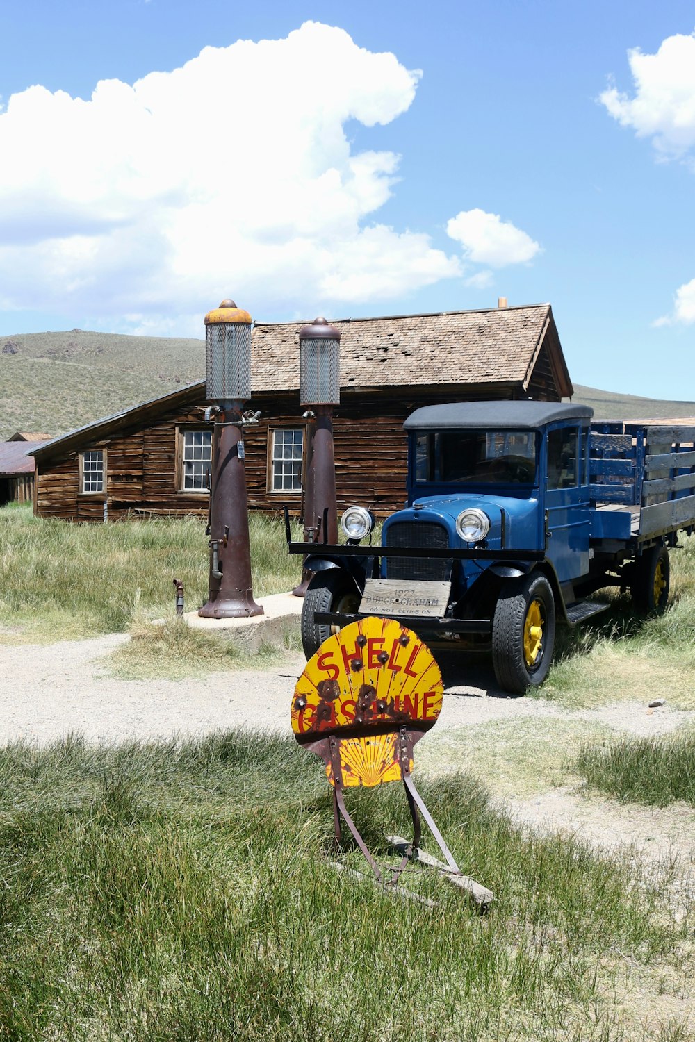 blauer und gelber Oldtimer tagsüber neben einem braunen Holzhaus geparkt