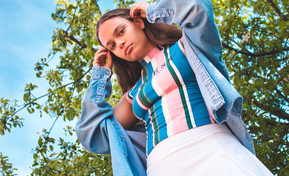 woman in white red and blue striped shirt and blue denim jeans sitting on green grass