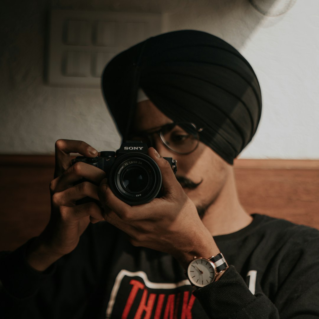 man in black and white fitted cap holding black nikon dslr camera