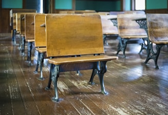 Classic wooden school desks with metal legs are arranged in rows on a polished hardwood floor, creating a nostalgic classroom setting.