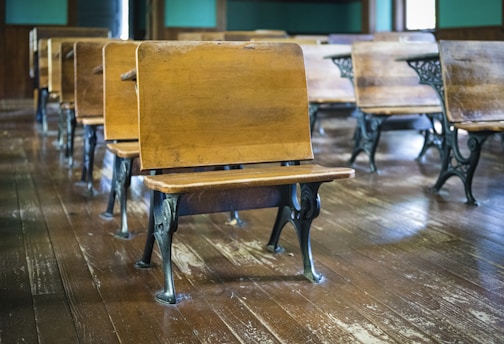 Classic wooden school desks with metal legs are arranged in rows on a polished hardwood floor, creating a nostalgic classroom setting.