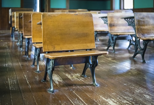 Classic wooden school desks with metal legs are arranged in rows on a polished hardwood floor, creating a nostalgic classroom setting.