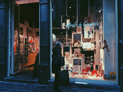 A person walks past a well-lit store window displaying various comic books, figurines, and colorful merchandise. The interior of the store is visible, showing shelves and decorations with a Tintin theme.