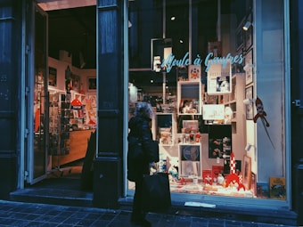A person walks past a well-lit store window displaying various comic books, figurines, and colorful merchandise. The interior of the store is visible, showing shelves and decorations with a Tintin theme.