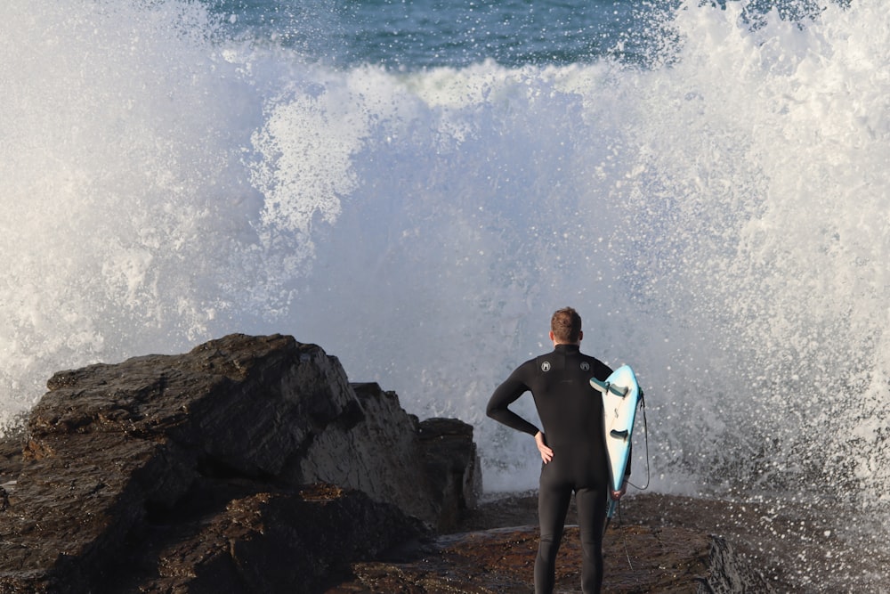 man in black shorts sitting on rock near ocean waves during daytime