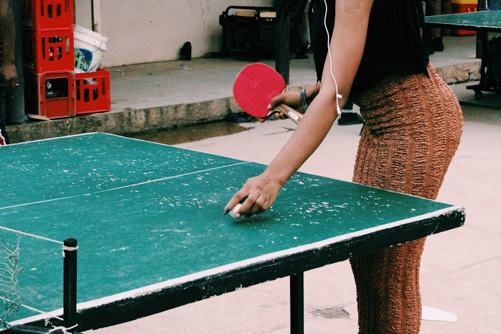 femme en débardeur marron tenant une raquette de tennis de table rouge et noire