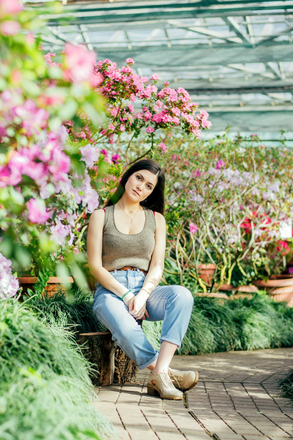 woman in brown tank top and blue denim jeans sitting on brown wooden bench