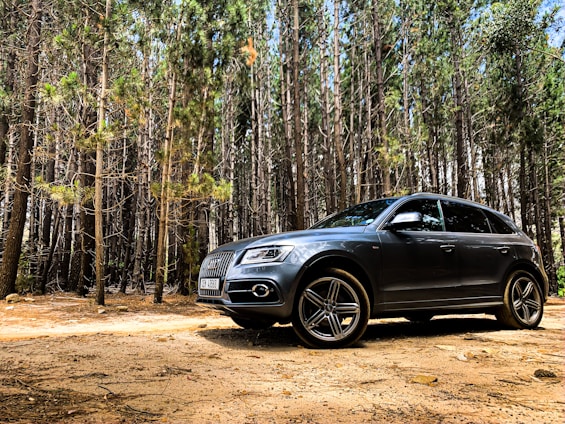A rugged black SUV parked on a forest trail with sunlight filtering through the trees