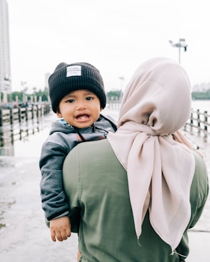 woman in green long sleeve shirt carrying baby in white and brown hijab