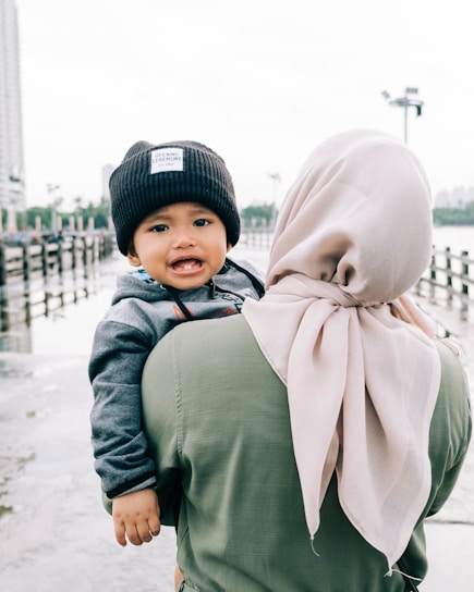 woman in green long sleeve shirt carrying baby in white and brown hijab