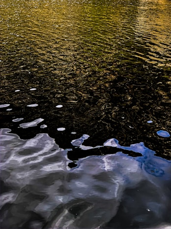 Rippled water surface reflecting golden and blue hues with white bubbles scattered across the water.
